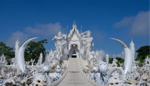 Vista frontal do Templo Branco com ponte e jardim em Chiang Rai